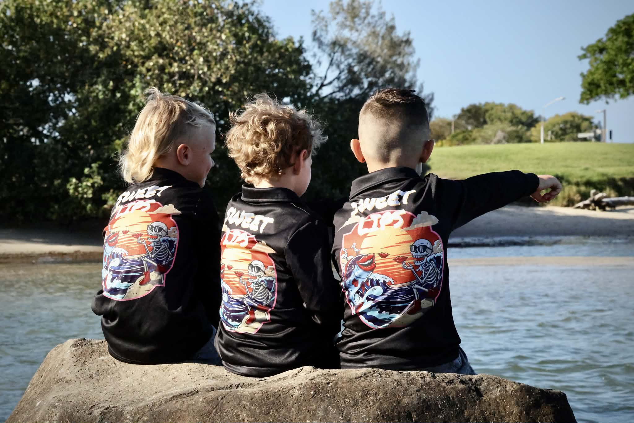 Three children wearing matching jackets with a colorful design sitting by a body of water.